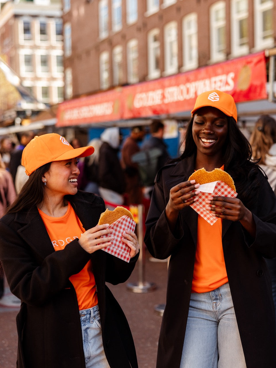 girls eating stroopwafel wearing orange program kings day caps and shirts